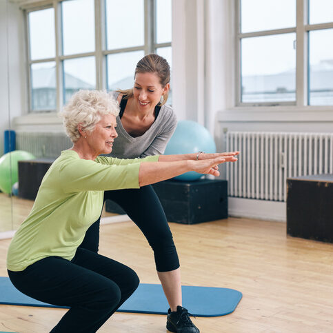 Elderly woman doing exercise with her personal trainer at gym. Gym instructor assisting senior woman in her workout.